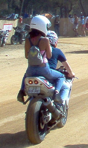 A bike with a girl on the back wearing jeans and a skimpy top and a helmet